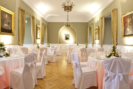 Saal mit olivgrünen Wänden, weißen Stuhlhussen und Beleuchtung unter den Tischen