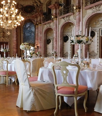 Eingedeckter Festsaal mit Blumenschmuck auf den Tischen und Stuhlhussen